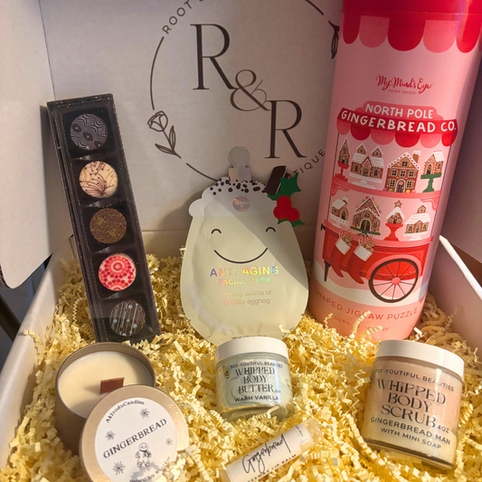 Assorted holiday products including a winter candle, whipped body butter, whipped body scrub, anti-aging korean skincare face mask, lip balm, chocolate truffles, and a Gingerbread Cart Holiday Puzzle